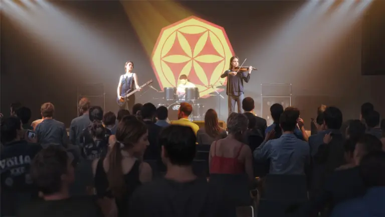 Band mit Sängerin, Schlagzeuger und Gitarrist auf einer Bühne während eines Konzerts mit Lichtern und Publikum.